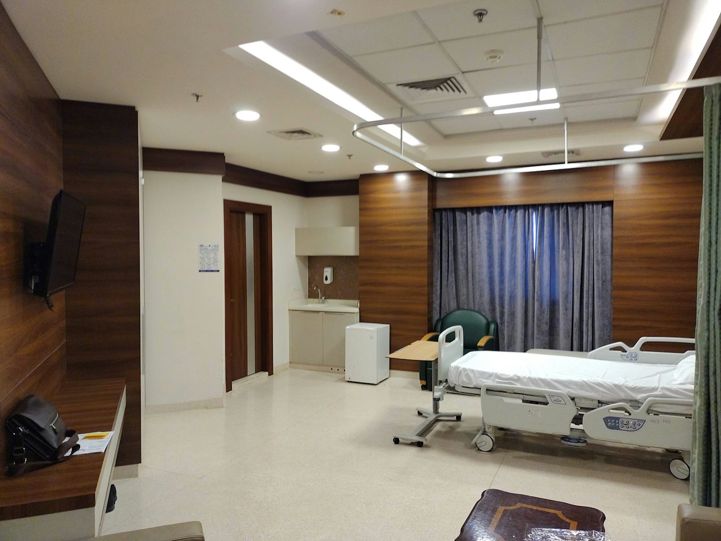 A modern hospital room with a bed, armchair, and sink.